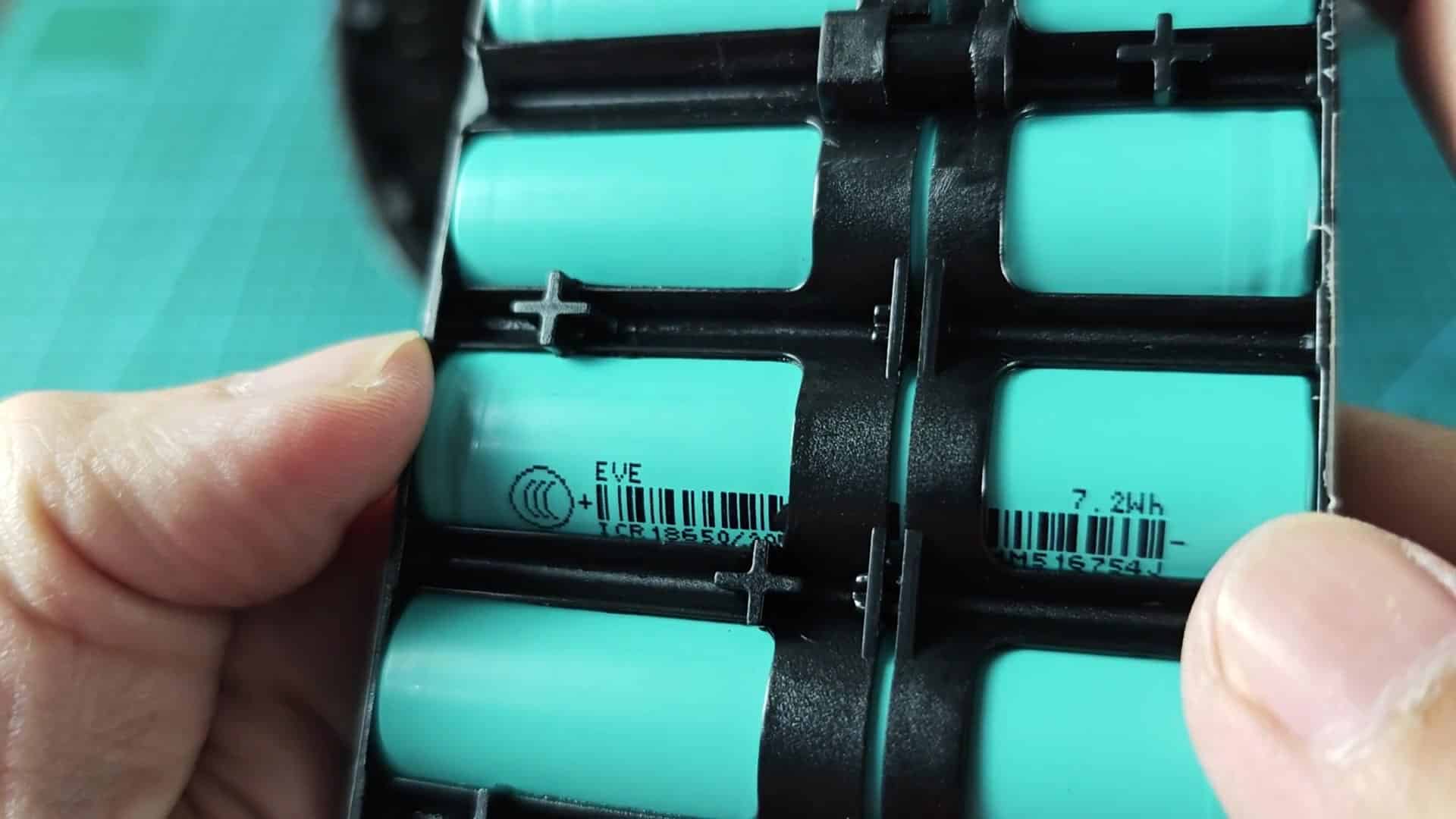 Opened device housing on a green cutting mat; a finger points toward an internal white rectangular foam/filter block beside bundled colored wires (yellow, blue, red, purple) and a small circuit board area Opened device housing on a green cutting mat; a finger points toward an internal white rectangular foam/filter block beside bundled colored wires (yellow, blue, red, purple) and a small circuit board area