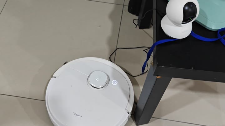 Powered on Deebot vacuum next to table Powered on Deebot vacuum next to table